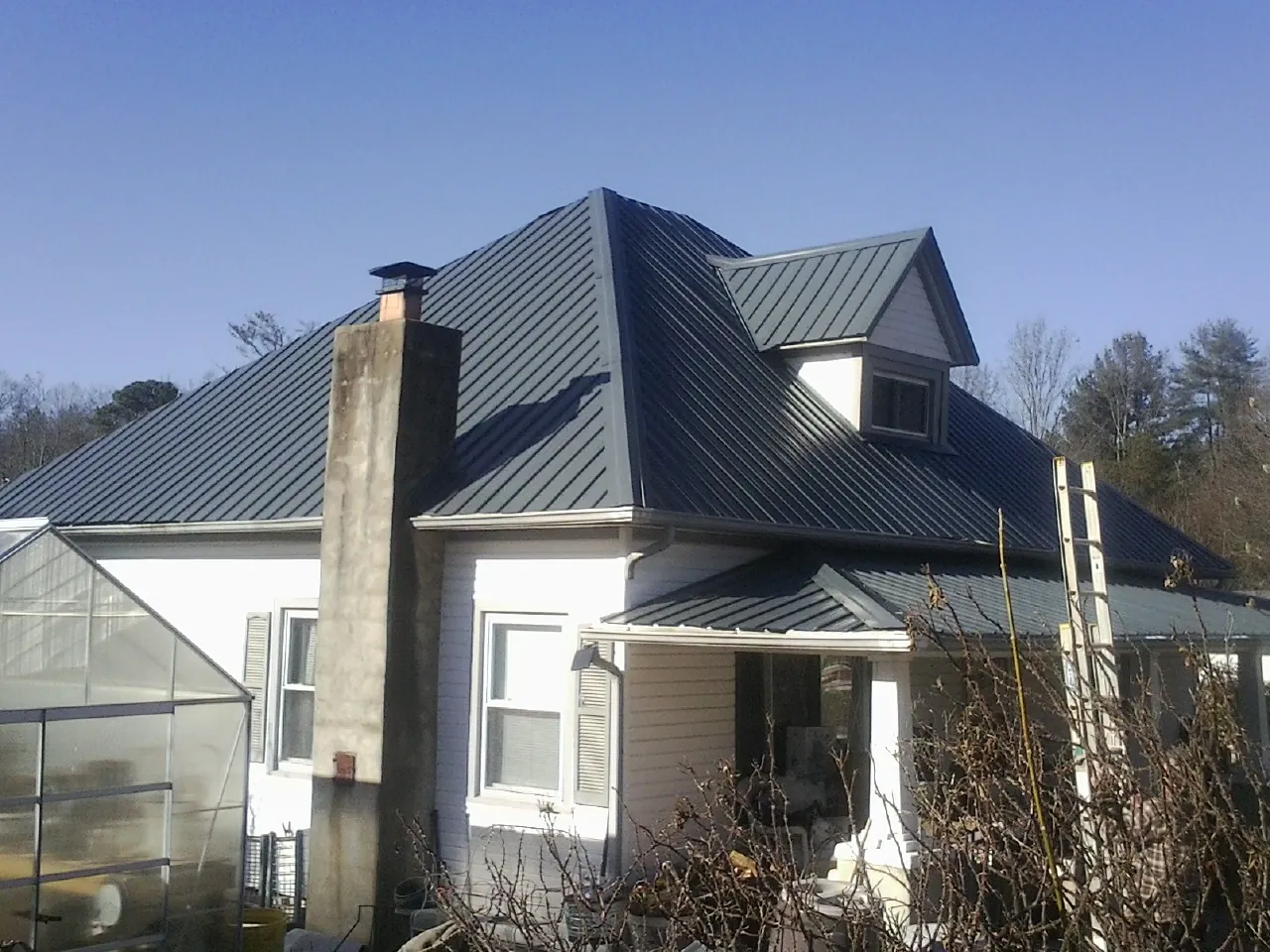 Dark blue standing seam metal roof on a white farmhouse with dormer — Slate & Tile Roof Repair by Roofing Brothers in Rockwood